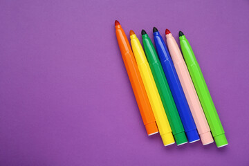 Different colorful markers on purple background, flat lay. Space for text
