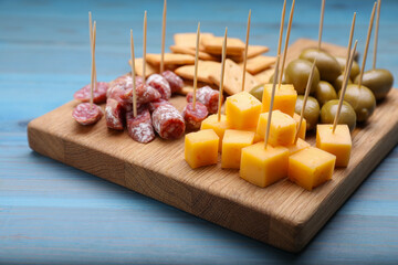 Toothpick appetizers. Pieces of cheese, sausage, olives and crackers on light blue wooden table,...