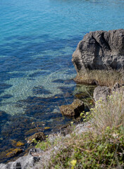Beach coast with a view over the sea with some mountains in the background and rocks in the water.