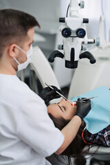 Skilled user. Handsome young male dentist looking into the lens of a professional microscope and...