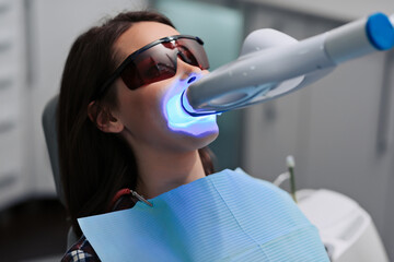 Close-up portrait of a female patient at dentist in the clinic. Teeth whitening procedure with...