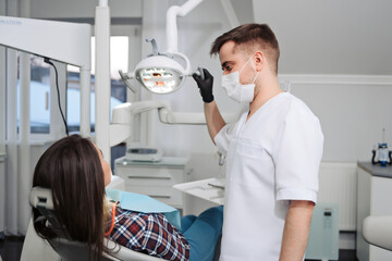 Dentist in mask and uniform consulting his patient in dental clinic.