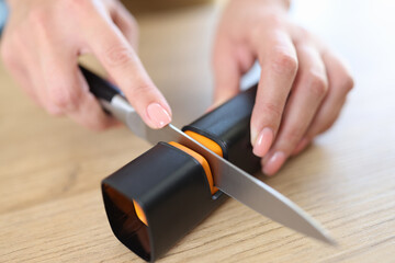Woman hands sharpen knife with sharpener on kitchen table close-up.