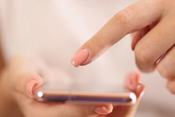 Close-up woman holding mobile phone, one finger above screen of phone.