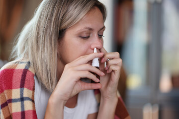 Fototapeta na wymiar Sad woman with illness uses nasal spray while sitting at home close-up.