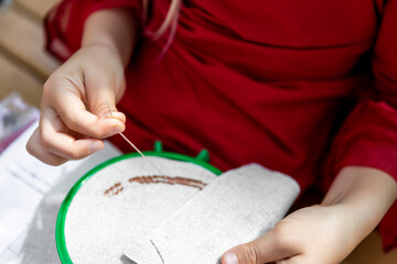 Close-up detail female child hands embroidering round hoop fabric frame with cross-stitch . Girl person handmade craft sewing pattern on canvas. Children development fine motor skills hobby artwork