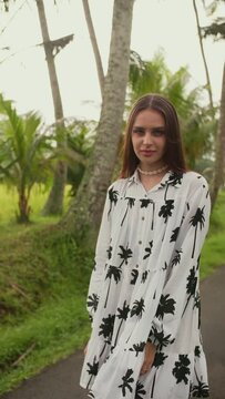 vertical video brunette poses in a dress against the background of palm trees