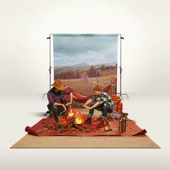 Two mates, men recreating camping activity over grey background with nature wallpaper. Paper fire. Imagination