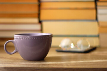 Cup of tea or coffee, e-reader and reading glasses on the table. Pile of books in the background. Selective focus.