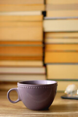 Cup of tea or coffee, e-reader and reading glasses on the table. Pile of books in the background. Selective focus.