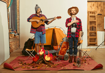 Singing anthem. Two men imagining, recreating camping activity indoors with necessary equipment....