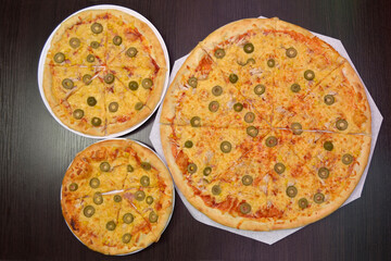 Three delicious fresh cheese pizzas with ham, olives on black table, three different sizes for serving in pizzeria