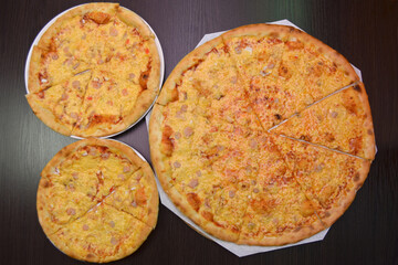 Three delicious fresh cheese pizzas with shrimp on black table, three different sizes for serving in pizzeria