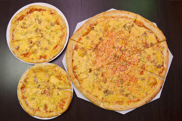 Three delicious fresh cheese pizzas with fish, lemon on black table, three different sizes for...
