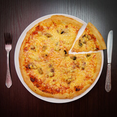 Delicious fresh round cheese pizza with mussels on black table, surface, on white plate, fork, knife nearby, top view