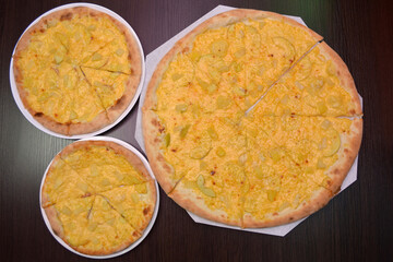 Three delicious fresh round cheese pizzas with pear, pineapples on a black table, surface, on a white plates, three different sizes for serving in a pizzeria