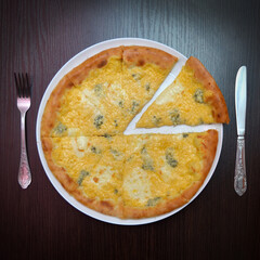 Delicious fresh round four cheeses pizza on black table, surface, on white plate, fork and knife nearby, top view