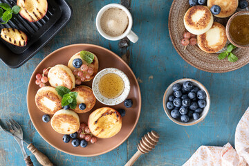 Cottage cheese pancakes, cheesecakes, ricotta fritters with fresh blueberries, currants and peaches on a plate. Healthy and delicious breakfast for the holiday. Blue wooden background
