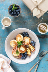 Cottage cheese pancakes, cheesecakes, ricotta fritters with fresh blueberries, currants and peaches on a plate. Healthy and delicious breakfast for the holiday. Blue wooden background
