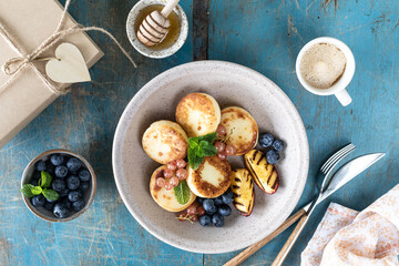 Fototapeta na wymiar Cottage cheese pancakes, cheesecakes, ricotta fritters with fresh blueberries, currants and peaches on a plate. Healthy and delicious breakfast for the holiday. Blue wooden background