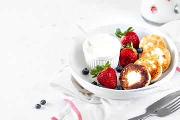 Cottage cheese pancakes, cheesecakes, ricotta fritters with fresh strawberries and blueberries from a white ceramic plate. Healthy and delicious breakfast for the holiday.