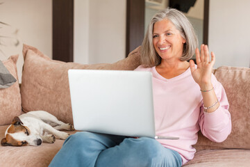 Middle aged smiling woman waving her hand to laptop