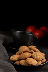 Close-up of plate with cookies, black cup and tangerines on dark table, black background, vertical, with copy space