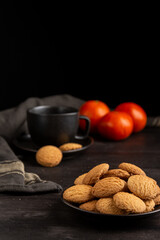 Top view of plate with cookies, black cup and tangerines on dark table, black background, vertical