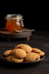 Top view of plate with cookies, spoon and jar of jam on dark table, selective focus, black background, vertical, with copy space