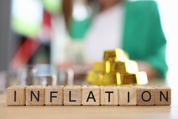 Word inflation collected from wooden cubes with gold bars and stacks of coins on office table.