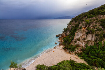 Sandy Beach on a rocky coast near Cala Gonone, Sardinia. Cloudy Sunrise Sky.