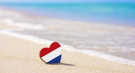 Flag of the Netherlands in the shape of a heart on a sandy beach.