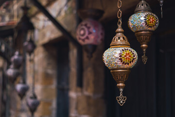 handmade traditional colorful Turkish lamps and lanterns, selective focus on lantern, blurred background, popular souvenir lanterns hanging in shop for sale.