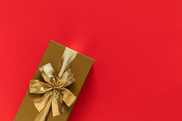 Golden gift box with golden ribbon and bow on a red background. Top view. Copy space.