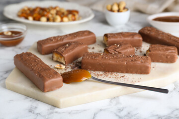 Board with delicious chocolate bars, caramel and nuts on white marble table