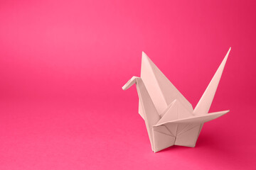 Origami art. Handmade paper crane on pink background, space for text