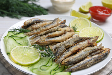Plate with delicious fried anchovies, lime and cucumber on table, closeup