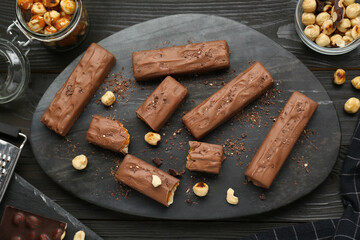 Board with delicious chocolate bars, caramel and nuts on black wooden table, flat lay