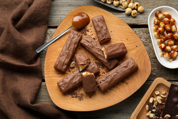 Tasty chocolate bars with caramel and nuts on wooden table, flat lay