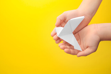 Origami art. Child holding paper bird on yellow background, top view. Space for text