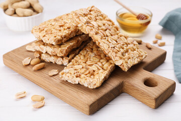 Board with tasty kozinaki bars, peanuts and honey on white wooden table