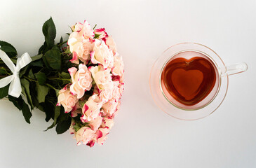 Herzförmige Teetasse aus Glas mit rotem Tee gefüllt auf weißem Hintergrund, ein Blumenstrauß...