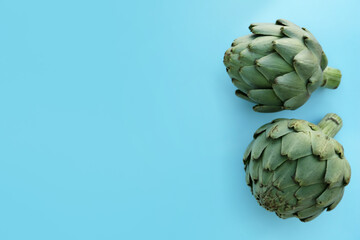 Obraz premium Whole fresh raw artichokes on light blue background, flat lay. Space for text