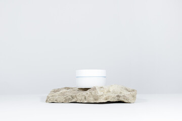 A mock up white jar of cream on a natural stone podium pedestal, on a white table, with hard shadows. Stylish look of the product, identity.