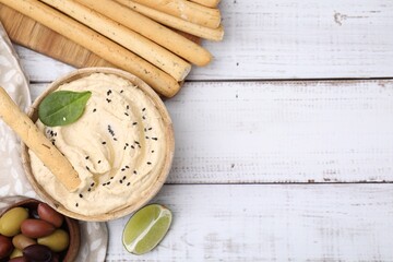Fototapeta na wymiar Delicious hummus with grissini sticks served on white wooden table, flat lay. Space for text