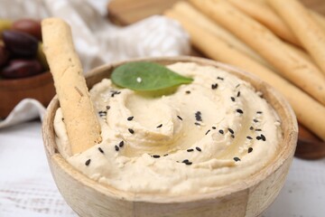 Fototapeta na wymiar Delicious hummus with grissini stick on white wooden table, closeup