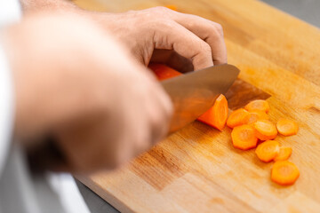 cooking food, profession and people concept - close up of male chef with knife chopping carrot on cutting board at restaurant kitchen