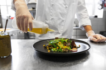 food cooking, profession and people concept - close up of male chef cook dressing plate of vegetable salad with olive oil at restaurant kitchen table