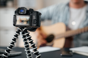 music, blogging and technology concept - close up of camera on tripod recording video or live streaming male guitarist or musician playing acoustic guitar at home
