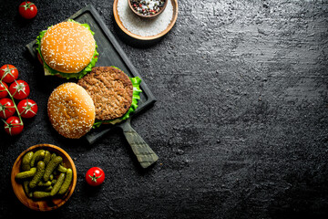 Burgers on a cutting Board with gherkins and spices in bowls.